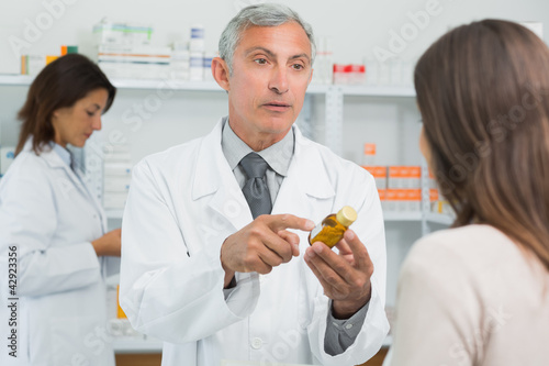 Photo: Pharmacist talking to a customer while holding a flask of pills Pharmacist talking to a customer while holding a flask of pills