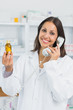 Smiling female pharmacist holding a bottle of pills while phoning