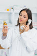 Female pharmacist looking at a bottle of pills while phoning