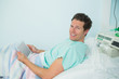 Smiling male patient touching a tactile tablet while lying on a bed
