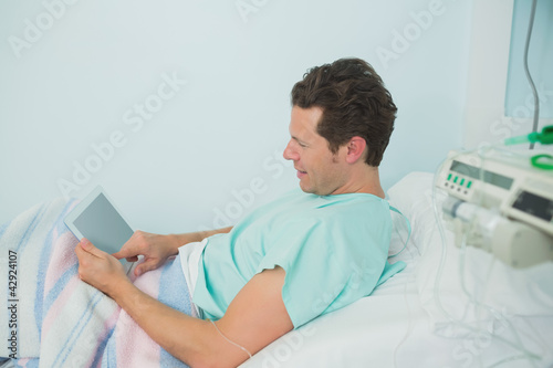 Photo: Male patient touching a tactile tablet while lying on a bed Male patient touching a tactile tablet while lying on a bed