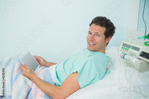 Photo: Smiling male patient touching a tactile tablet while lying on a bed Smiling male patient touching a tactile tablet while lying on a bed
