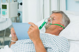 Photo: Senior male patient lying on a bed with a mask while holding a tactile tablet Senior male patient lying on a bed with a mask while holding a tactile tablet