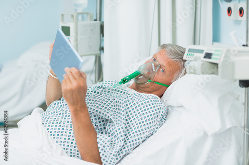 Photo: Senior patient holding a tactile tablet in his hands while wearing an oxygen mask Senior patient holding a tactile tablet in his hands while wearing an oxygen mask