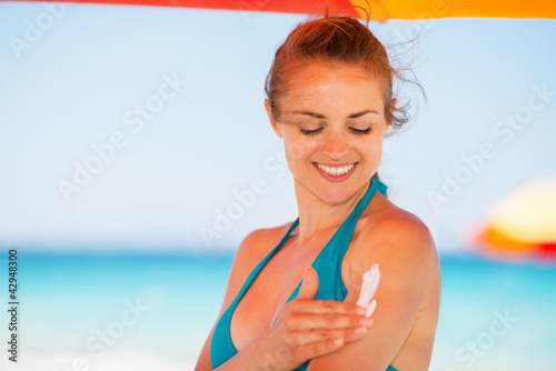 Photo: Happy woman applying sun screen creme on arm Happy woman applying sun screen creme on arm