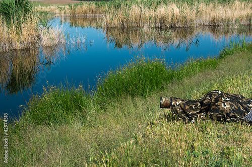 Foto: Camouflaged wild life photographer waiting for birds by lake Camouflaged wild life photographer waiting for birds by lake