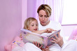 A woman sitting on the bed reading bedtime story for her daughter