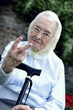 A bespectacled woman with headscarf and walking stick showing two fingers