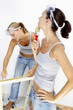 A woman measuring a wood while her friend is checking the paint on the wall