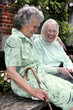 Two old women having fun sitting on the bench talking