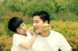 A boy playfully placing two green apples on his father's cheeks