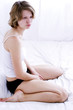 Side shot of a woman in white camisole sitting on the bed