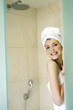 A woman with her hair and body wrapped up in towel hiding behind the shower door