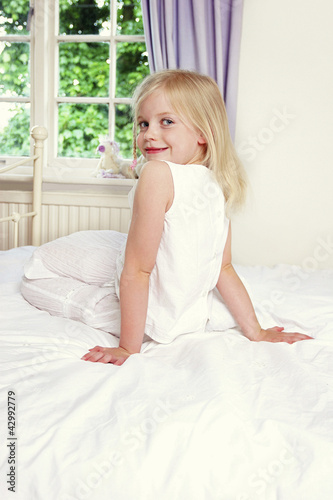 Photo: Back shot of a girl sitting on the bed while flashing a smile at the camera Back shot of a girl sitting on the bed while flashing a smile at the camera