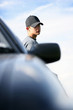 A boy with cap standing beside his car