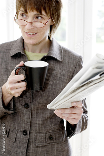 Photo: Woman with glasses holding cup and newspaper Woman with glasses holding cup and newspaper