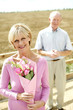 Foto: Senior woman holding a bouquet of flowers with her husband standing in the background Senior woman holding a bouquet of flowers with her husband standing in the background