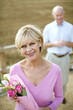 Foto: Senior woman holding a bouquet of flowers with her husband standing in the background Senior woman holding a bouquet of flowers with her husband standing in the background