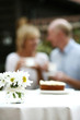 Focus on a vase of flowers with senior couple having tea in the background