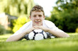 Teenage boy lying forward on the field with his chin resting on football