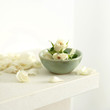 A bowl of white roses with a few petals scattered beside the bowl