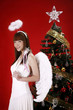 Young woman in angel costume standing beside Christmas tree