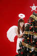 Young woman in angel costume standing beside Christmas tree