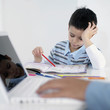 Boy doing homework while his father using laptop