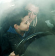 Boy sitting on father's lap holding steering wheel