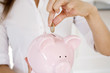 Businesswoman putting coin into piggy bank
