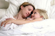 A woman and her daughter lying down on the bed looking at each other
