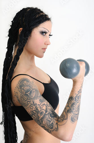 Photo: young tattooed stylish woman exercising with old dumbbells young tattooed stylish woman exercising with old dumbbells