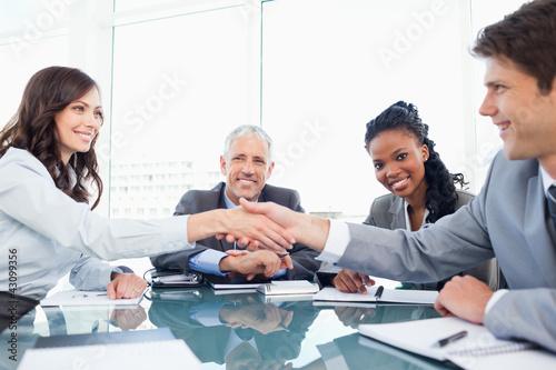 Photo: Two young executives shaking hands in front of their director an Two young executives shaking hands in front of their director an