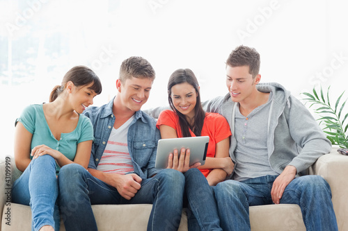 Foto: A group of friends sit on the couch while watching a tablet pc A group of friends sit on the couch while watching a tablet pc