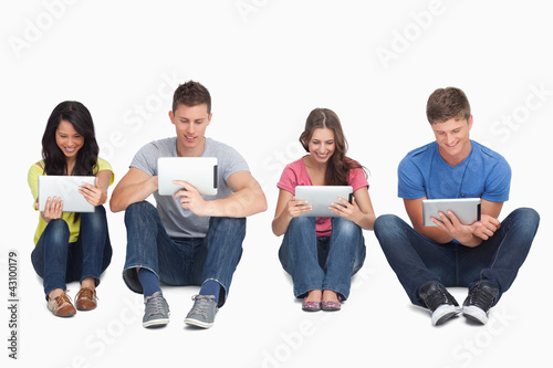 Foto: Four friends sitting on the ground all with tablets Four friends sitting on the ground all with tablets
