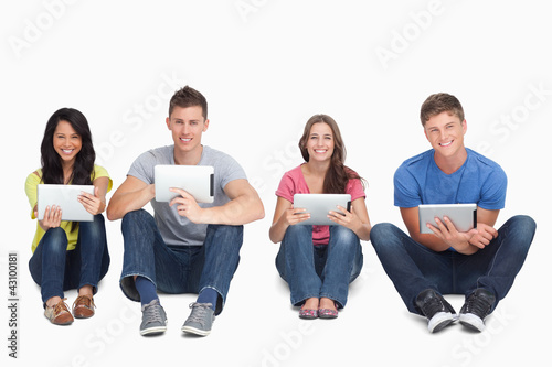 Photo: A group of people sitting beside each other with tablets while l A group of people sitting beside each other with tablets while l