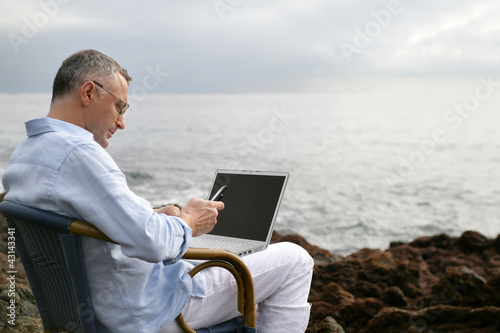 Foto: Man on a chair at the beach with his laptop Man on a chair at the beach with his laptop