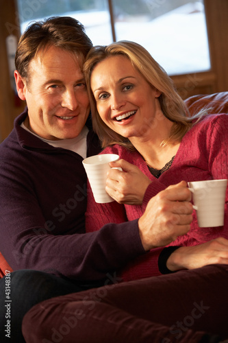 Photo: Middle Aged Couple Sitting On Sofa With Hot Drinks Middle Aged Couple Sitting On Sofa With Hot Drinks