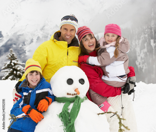Photo: Family Building Snowman On Ski Holiday In Mountains Family Building Snowman On Ski Holiday In Mountains