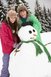 Two Teenagers Building Snowman On Ski Holiday In Mountains