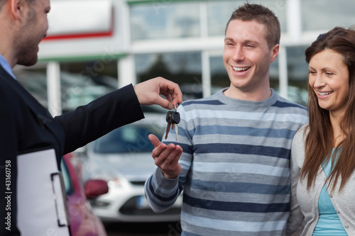 Photo: Couple receiving car keys by a dealer Couple receiving car keys by a dealer