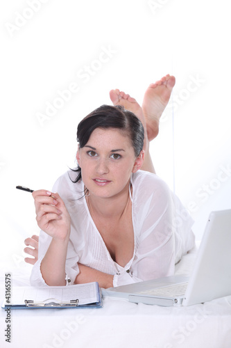 Photo: Young woman lying down with a laptop computer and clipboard Young woman lying down with a laptop computer and clipboard