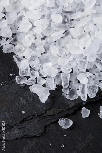 Photo: Coarse sea salt on black slate stone background, closeup Coarse sea salt on black slate stone background, closeup