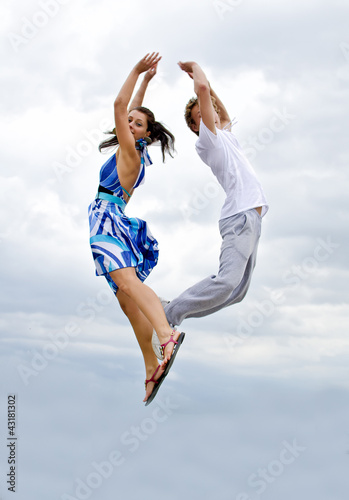 Photo: Portrait of a happy young couple jumping in air against sky. Portrait of a happy young couple jumping in air against sky.