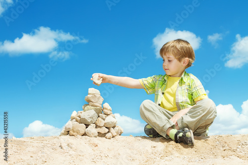 Foto: Child putting last stone part to pyramid sitting over sky Child putting last stone part to pyramid sitting over sky