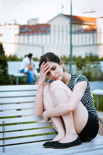 Photo: Depressed young woman sitting in a park full of happy couples Depressed young woman sitting in a park full of happy couples
