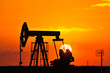 An oil pump jack is silhouetted by the setting sun