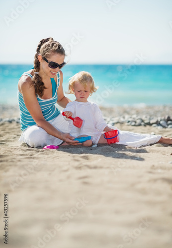 Photo: Mother and baby playing with sand on beach Mother and baby playing with sand on beach