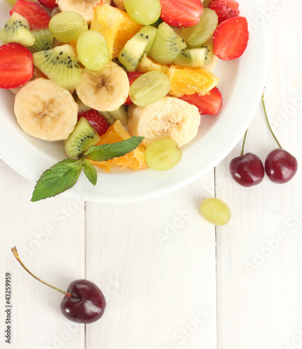 Photo: Fresh fruits salad on plate and berries on white wooden table Fresh fruits salad on plate and berries on white wooden table