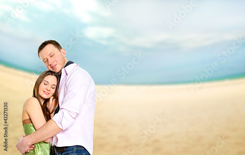 Photo: Portrait of young couple in love embracing at beach and enjoying Portrait of young couple in love embracing at beach and enjoying